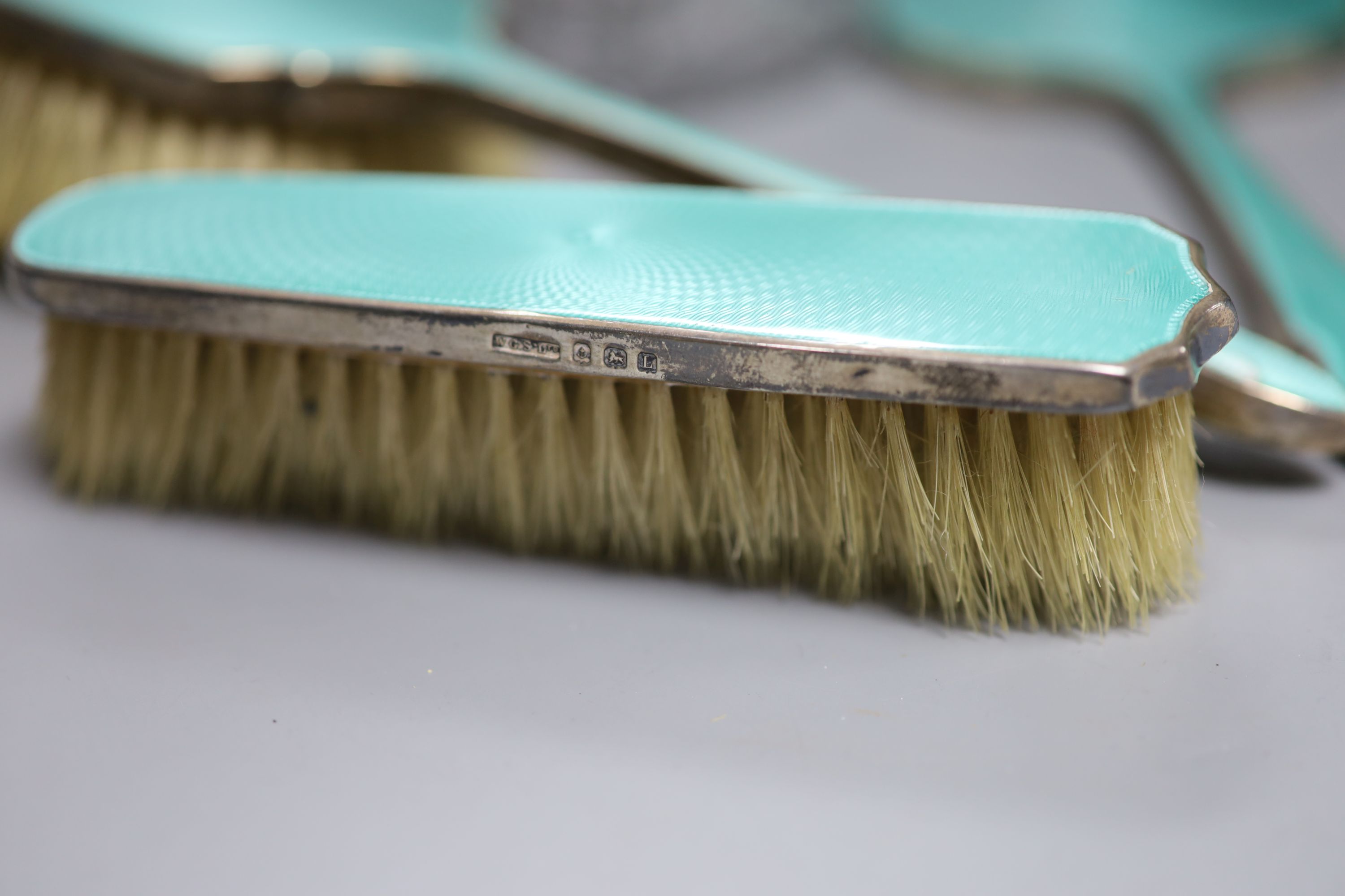 A 1930's silver and enamel toilet set including powder bowl, mirror and two brushes and one other silver & enamel brush.